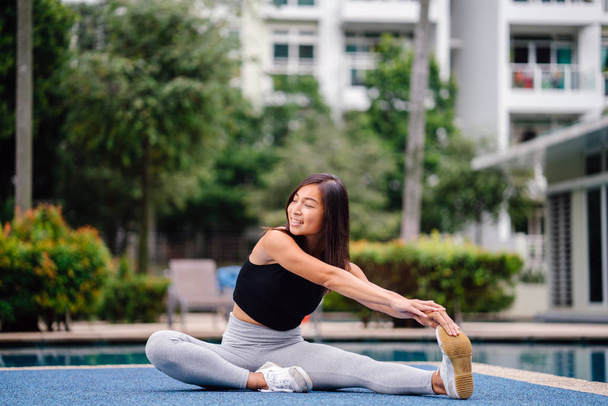 Portrait of an attractive, young Chinese Asian woman dressed in sporty, active wear  doing exercises near pool during the day on the weekend. - Zdjęcie, obraz