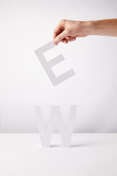 cropped view of person holding paper letters - e and w, on white background - Zdjęcie, obraz