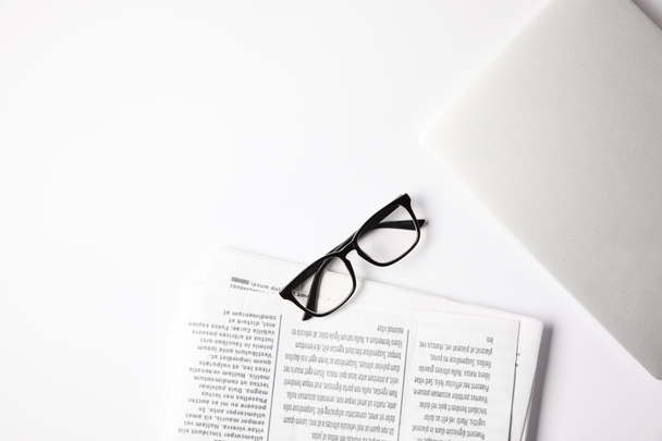 top view of eyeglasses, laptop and newspapers on white table - Foto, Imagem