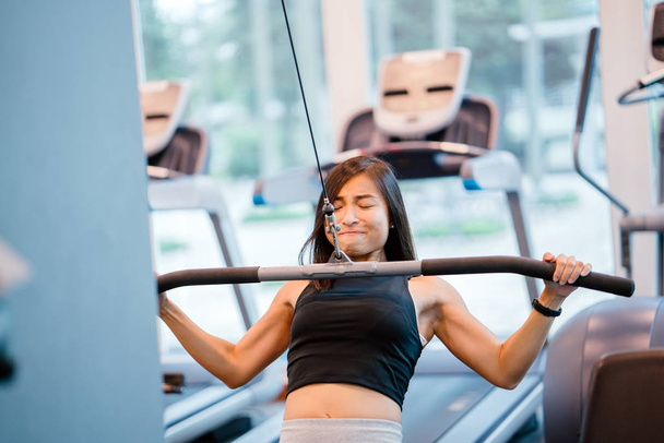 Portrait of a young, Chinese Asian woman working out in the gym. She is working with heavy weights and she is lean, tanned, toned and muscular. She is very focused on her workout. - Foto, Imagem