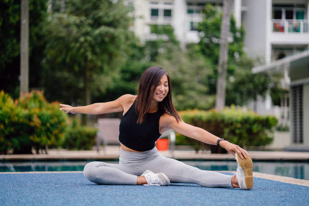 Portrait of an attractive, young Chinese Asian woman dressed in sporty, active wear  doing exercises near pool during the day on the weekend. - Foto, afbeelding