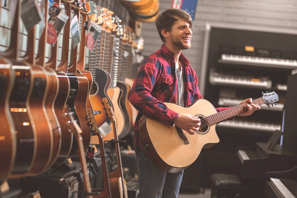Молодой человек играет на гитаре в магазине
 - Фото, изображение