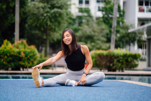 Portrait of an attractive, young Chinese Asian woman dressed in sporty, active wear  doing exercises near pool during the day on the weekend. - Foto, imagen
