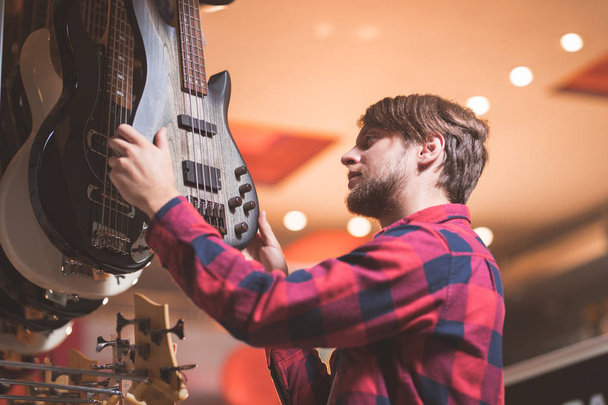 A young man chooses a guitar in a store - Photo, Image