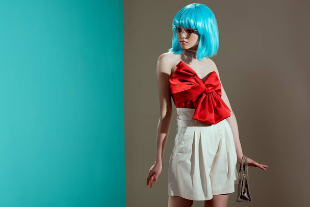 attractive young female model in blue wig and red bow looking away in studio - 写真・画像