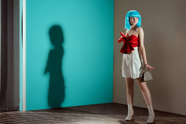 Вид в полный рост красивой стильной девушки в синем парике, позирующей и отводящей взгляд в студии
  - Фото, изображение