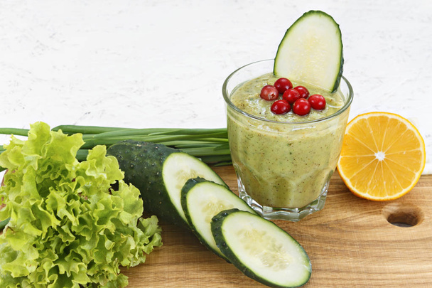 The concept of purification from detoxification, the ingredients of a green vegetable cocktail. Natural, organic healthy juice in a bottle for a diet for weight loss or fasting. Cucumber, lemon and lettuce, cranberry, green onion isolated on white wo - Foto, imagen