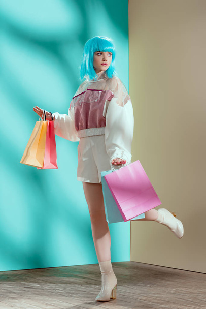 full length view of beautiful stylish young female model in blue wig holding shopping bags and looking away - Fotografie, Obrázek