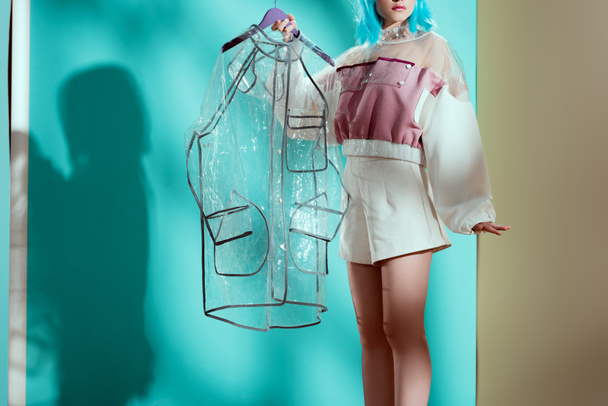 cropped shot of stylish female model in blue wig holding transparent raincoat - Fotoğraf, Görsel