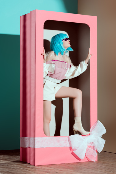 fashionable beautiful girl in blue wig posing in decorative pink box with bow  - Photo, Image