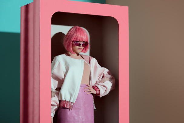 beautiful fashionable girl in pink wig posing with hand on waist in decorative box  - Fotó, kép