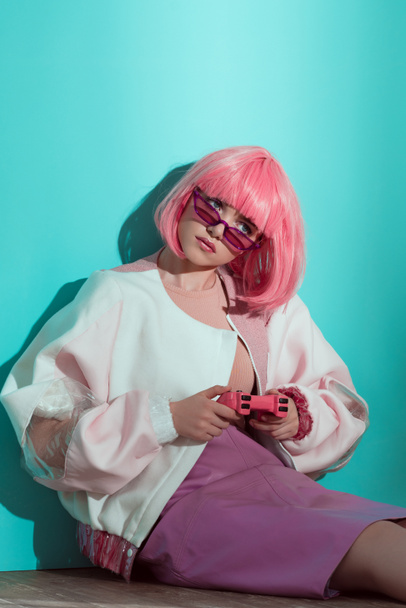 fashionable pretty girl in pink wig sitting on floor and playing with pink joystick - Zdjęcie, obraz