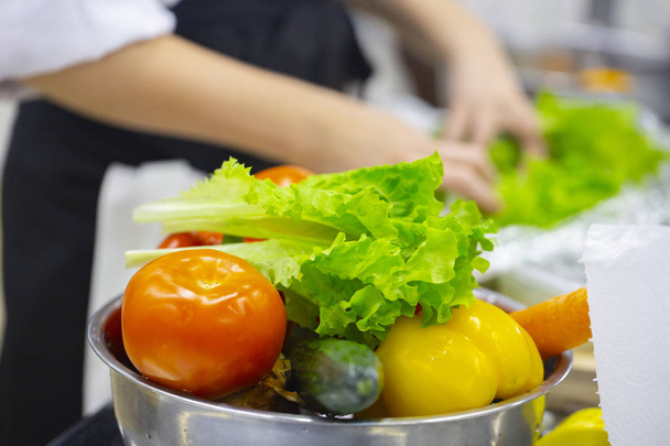 abgeschnittene Ansicht von Köchin wäscht Kräuter Schwerpunkt auf frisch gewaschenem Gemüse. - Foto, Bild