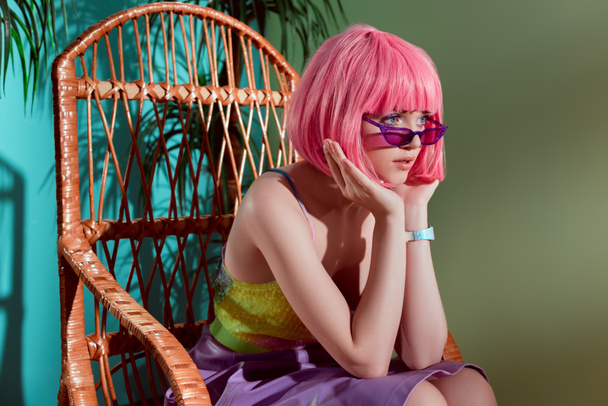 beautiful fashionable young female model in pink wig sitting in rocking chair and looking away - Foto, immagini