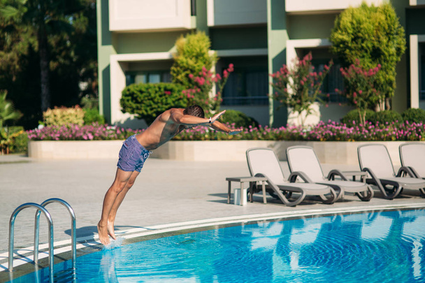 Young man jumping in swimming pool at resort - Foto, afbeelding