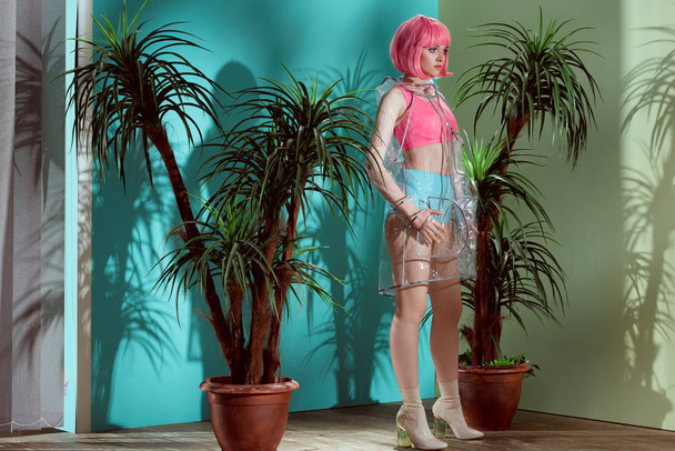 magnifique modèle féminin en perruque rose et imperméable transparent posant en studio
  - Photo, image