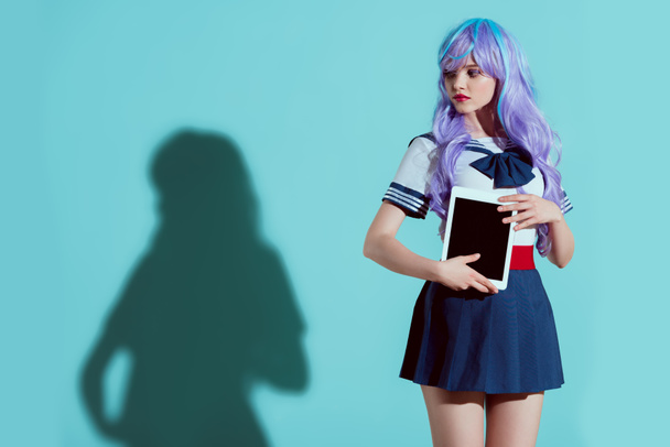stylish girl in bright wig holding digital tablet with blank screen and looking away on blue - Photo, image