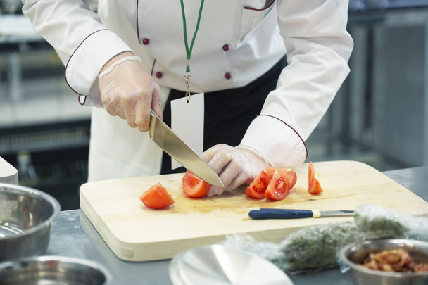 Χέρι με μαχαίρι κόβει ντομάτα. Κόκκινο λαχανικό στον πίνακα μαγειρέματος. - Φωτογραφία, εικόνα