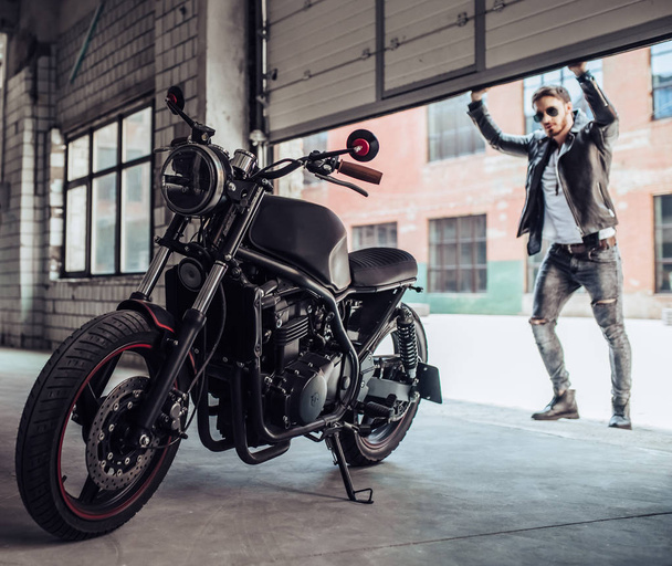 Handsome bearded biker with classic style black motorcycle. Cafe racer in garage. - Valokuva, kuva