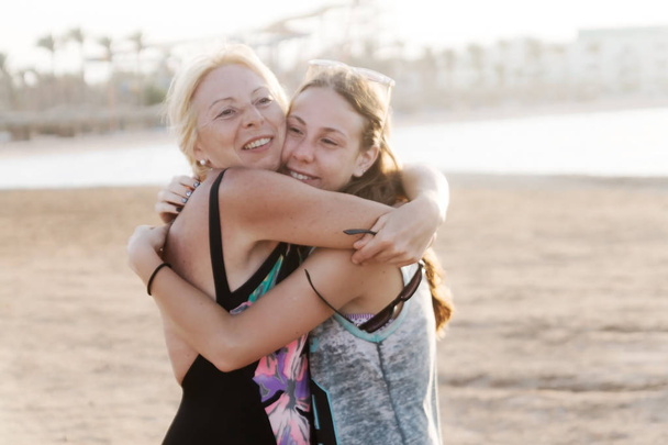 Cute pretty teen daughter with mature mother hugging in nature at sunset. - Photo, Image