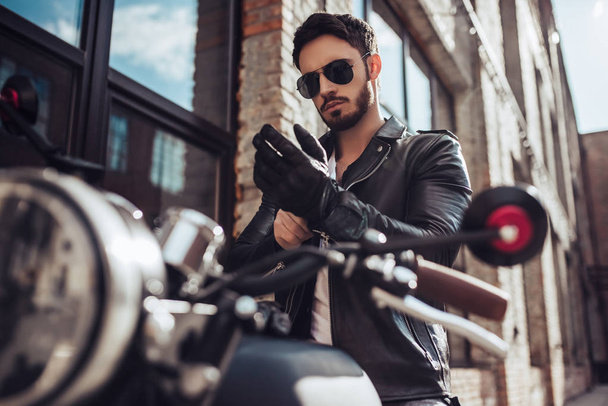 Handsome bearded biker with classic style black motorcycle. Cafe racer. - Foto, afbeelding