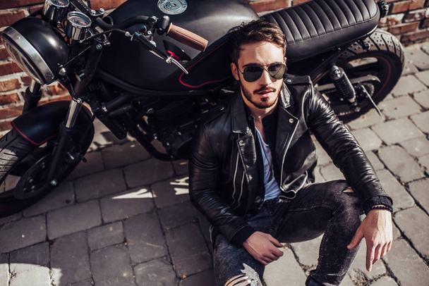 Handsome bearded biker with classic style black motorcycle. Cafe racer. - Foto, immagini