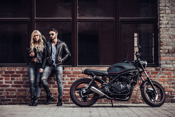 Romantic biker couple with black motorcycle. Handsome bearded man and young attractive woman outdoors with cafe racer. - 写真・画像