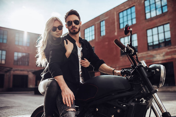 Romantic biker couple with black motorcycle. Handsome bearded man and young attractive woman outdoors with cafe racer. - Photo, Image