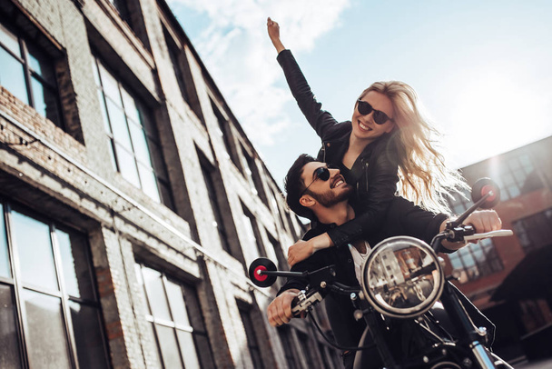 Romantic biker couple with black motorcycle. Handsome bearded man and young attractive woman outdoors with cafe racer. - Fotó, kép