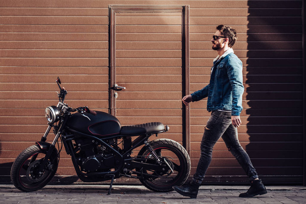 Handsome bearded biker with classic style black motorcycle. Cafe racer. - Фото, изображение