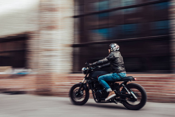 Handsome bearded biker with classic style black motorcycle. Cafe racer in motion. - Foto, Imagen