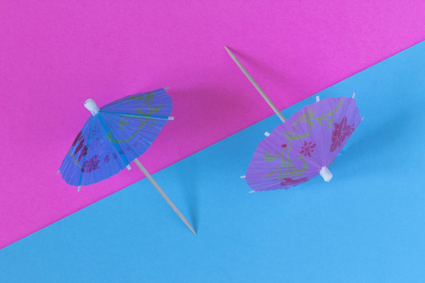 Creative view of a cocktail umbrella on a two-tone background - pink and blue. Conceptual image of summer. Minimalism. Abstraction. Summertime. Top view.  - Photo, Image