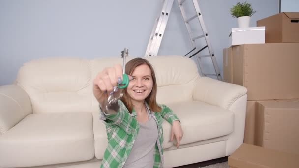 junge Frau sitzt mit Kartons und hält Wohnungsschlüssel in der Hand - Filmmaterial, Video