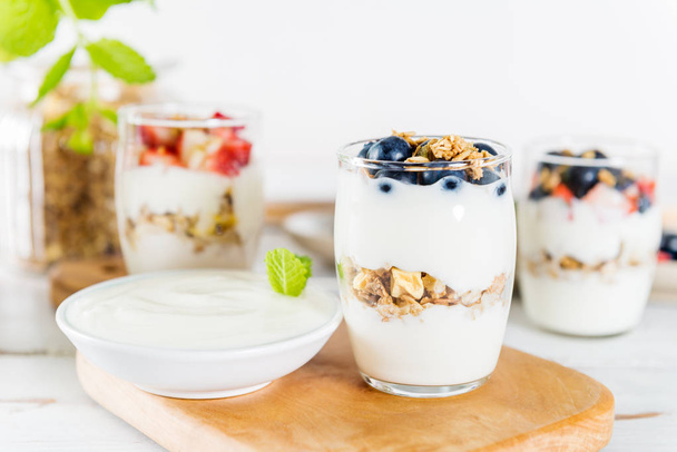 Frascos com sobremesa em camadas de iogurte natural, granola e morangos frescos e mirtilos em fundo de madeira
 - Foto, Imagem