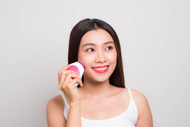 Skin Care. Side portrait of the charming healthy fresh woman with natural make-up using the electric facial massager at isolated white background. - Photo, Image