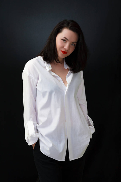 Γυναίκα που ποζάρει στο λευκό πουκάμισο μαύρο φόντο βλέμμα στην κάμερα - Φωτογραφία, εικόνα