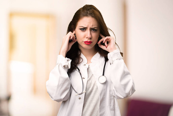 Doctor woman covering her ears on unfocused background - 写真・画像