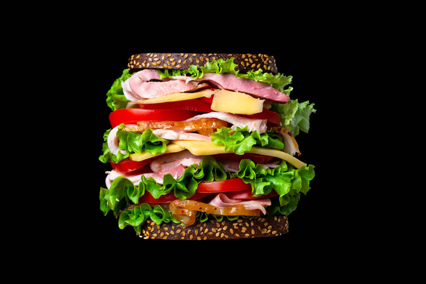 Huge appetizing sandwich on a black background. Isolated - Foto, immagini