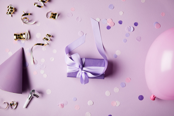 vista superior de una caja de regalo violeta, globo, sombrero de fiesta y piezas de confeti en la superficie
 - Foto, Imagen