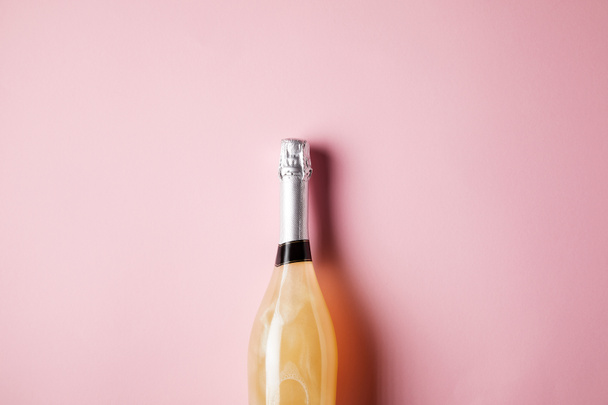 fles champagne op roze oppervlak (bovenaanzicht) - Foto, afbeelding