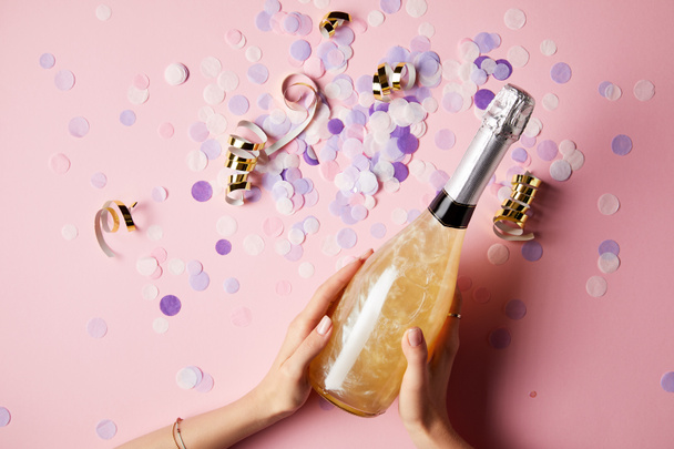 abgeschnittenes Bild einer Frau, die eine Flasche Champagner über Konfetti auf dem Partytisch hält - Foto, Bild