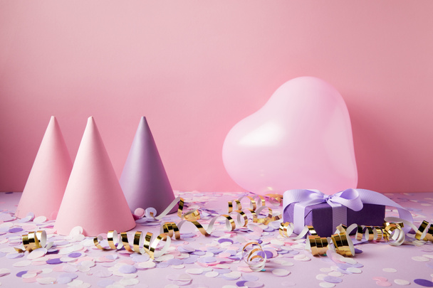 heart shaped balloon, party hats and present on violet tabletop - Photo, Image