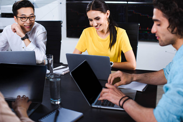 sorridente gruppo multiculturale di business partner che parla a tavola con i computer portatili in ufficio moderno
  - Foto, immagini
