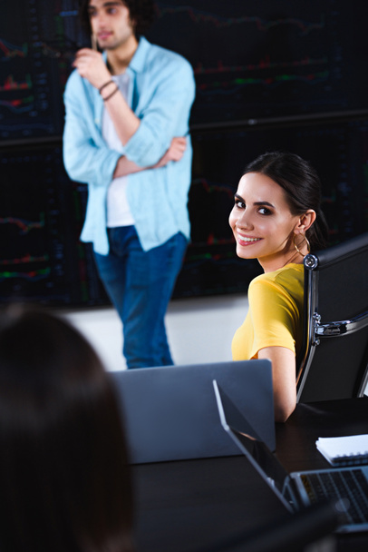 молодая улыбающаяся деловая женщина смотрит в камеру, в то время как ее деловой партнер показывает презентацию в современном офисе
  - Фото, изображение