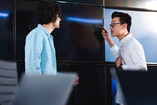 азіатський бізнесмен в окулярах вказує ручкою на колегу в сучасному офісі
 - Фото, зображення