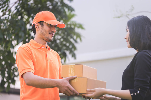 Чоловік в помаранчевому кольорі передає пакунки жінці
 - Фото, зображення