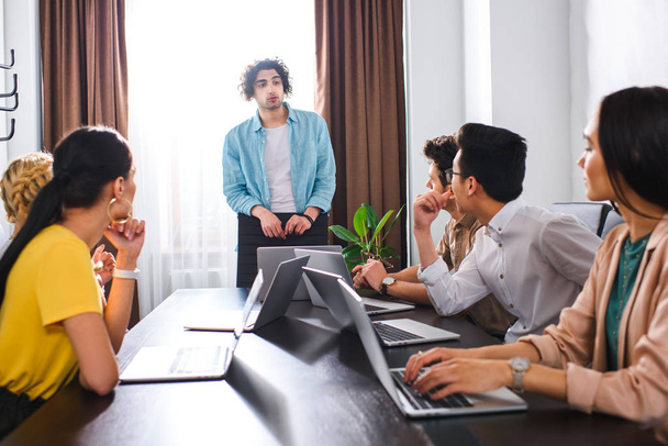 empresarios multiétnicos sentados a la mesa con ordenadores portátiles durante la reunión en la oficina moderna
  - Foto, imagen