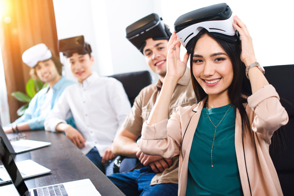 мультиэтнические деловые партнеры с гарнитурами виртуальной реальности за столом с ноутбуками в современном офисе
  - Фото, изображение