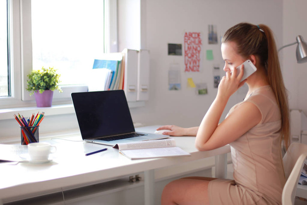Young businesswoman sitting at the desk and talking on phone - Foto, Bild