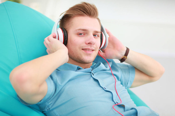 Un joven guapo en el sofá escuchando música - Foto, imagen